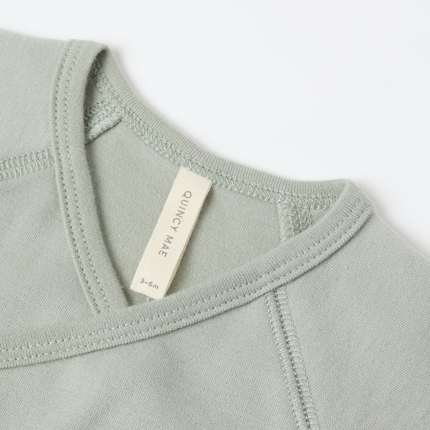 Close-up of a fern green baby outfit with a Quincy Mae label on a white background