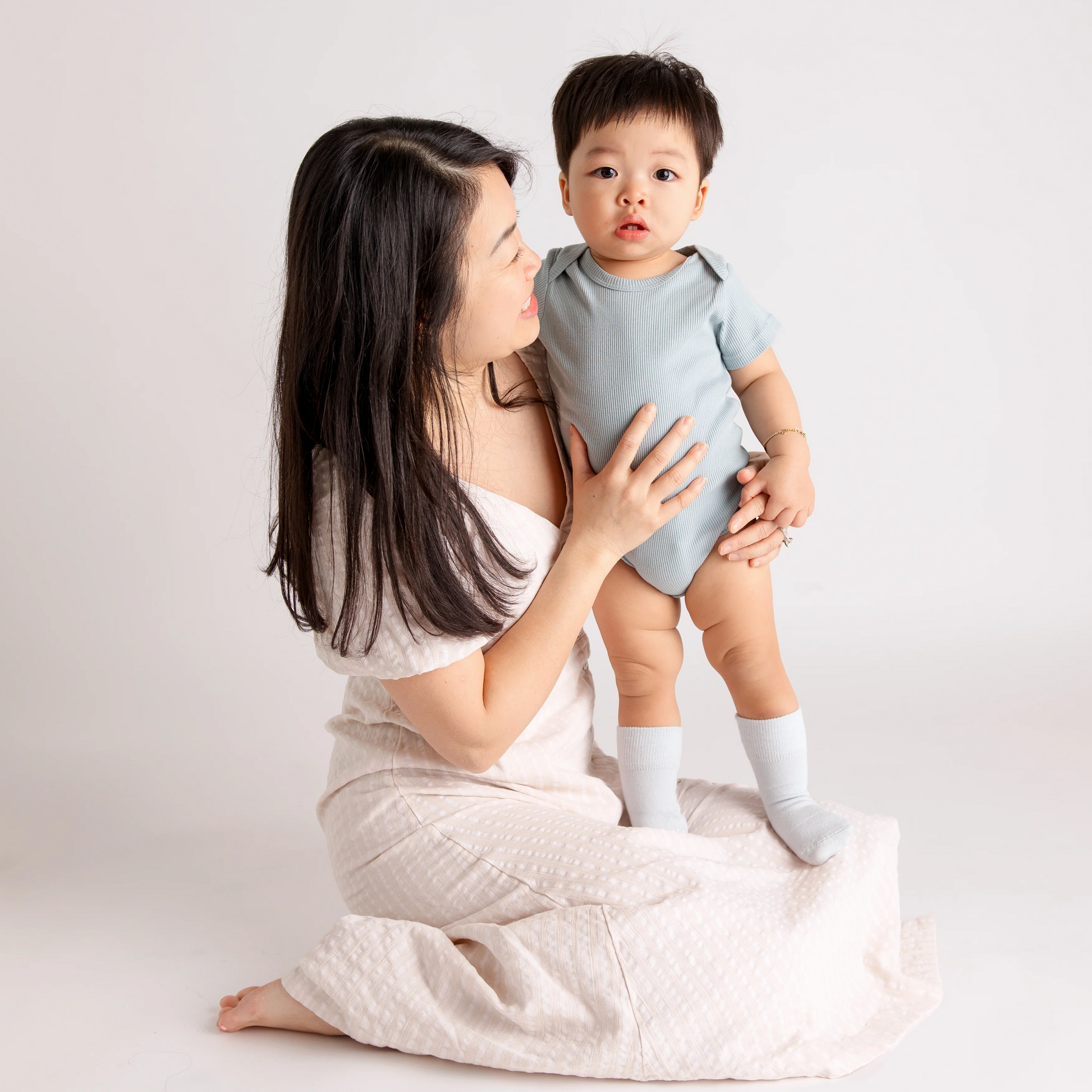 Dark long haired female holding young boy on her knees in blue bodysuit and ivory colored squid socks