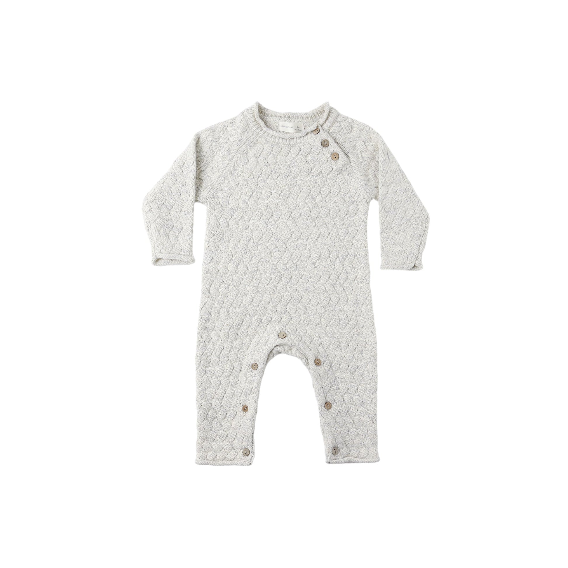Knit infant jumpsuit with a subtle pattern with coconut buttons on a white background